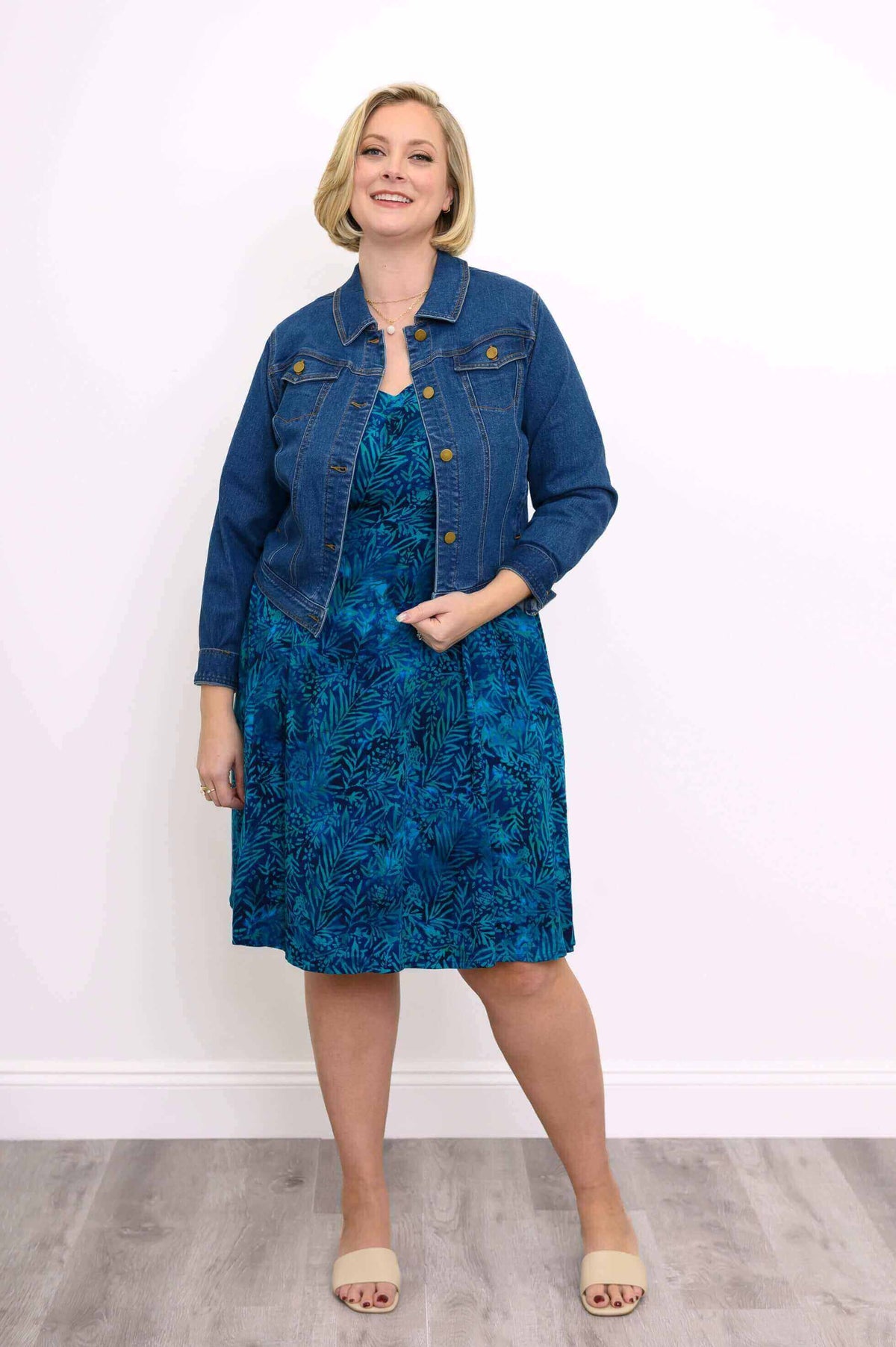 Woman pairing blue leaf print dress with denim jacket and slides
