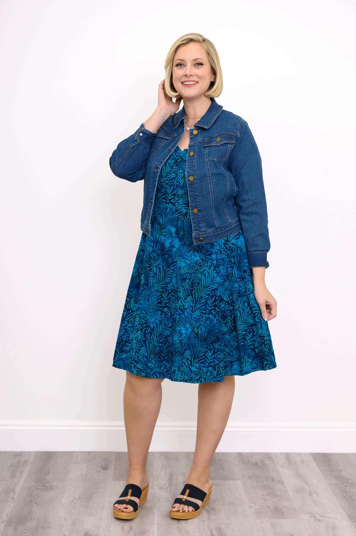 Model styling a blue tropical print A-line dress with a denim jacket and sandals