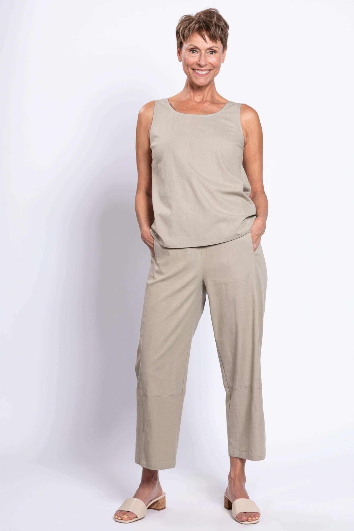 Woman wearing cropped beige Boardwalk Pants and matching sleeveless top, front view, hands in pockets