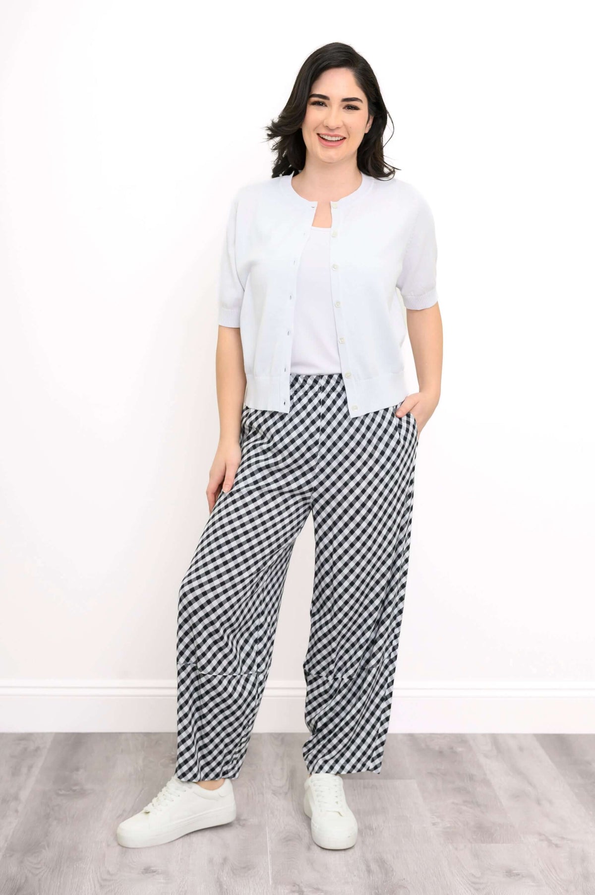 Woman wearing boardwalk black gingham barrel-leg pants styled with a white cardigan and sneakers
