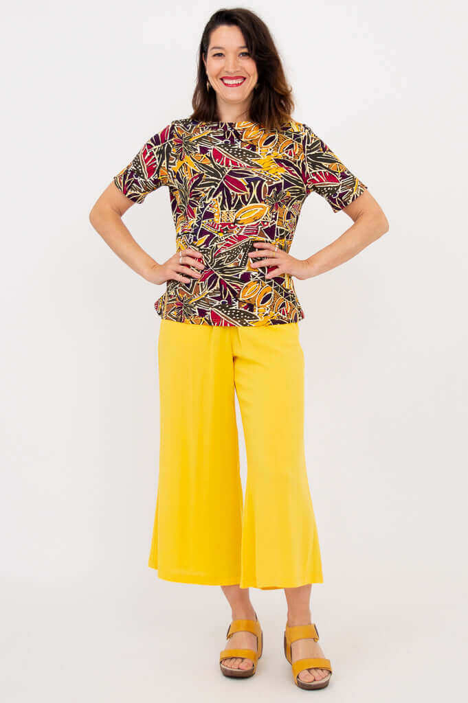 Full view of woman in botanical boatneck tee and yellow wide-leg pants, hands on hips