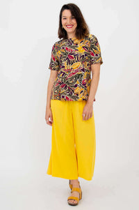 Woman posing in botanical print tee and bright yellow pants, looking confident