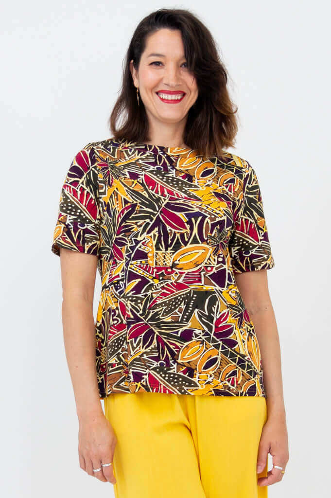 Woman wearing a vibrant botanical print boatneck tee with yellow pants, smiling