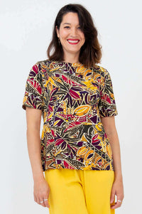 Woman wearing a vibrant botanical print boatneck tee with yellow pants, smiling