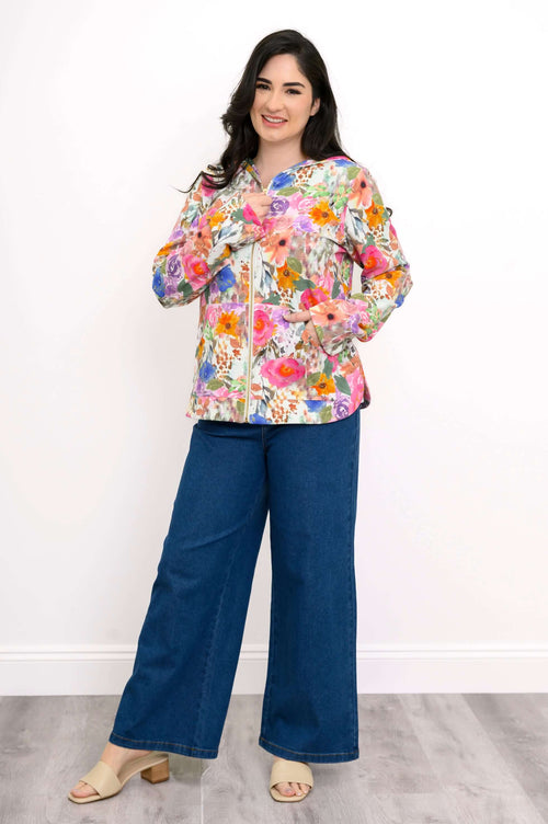 Woman wearing a colorful floral hoodie with jeans and sandals, posing with hands at collar