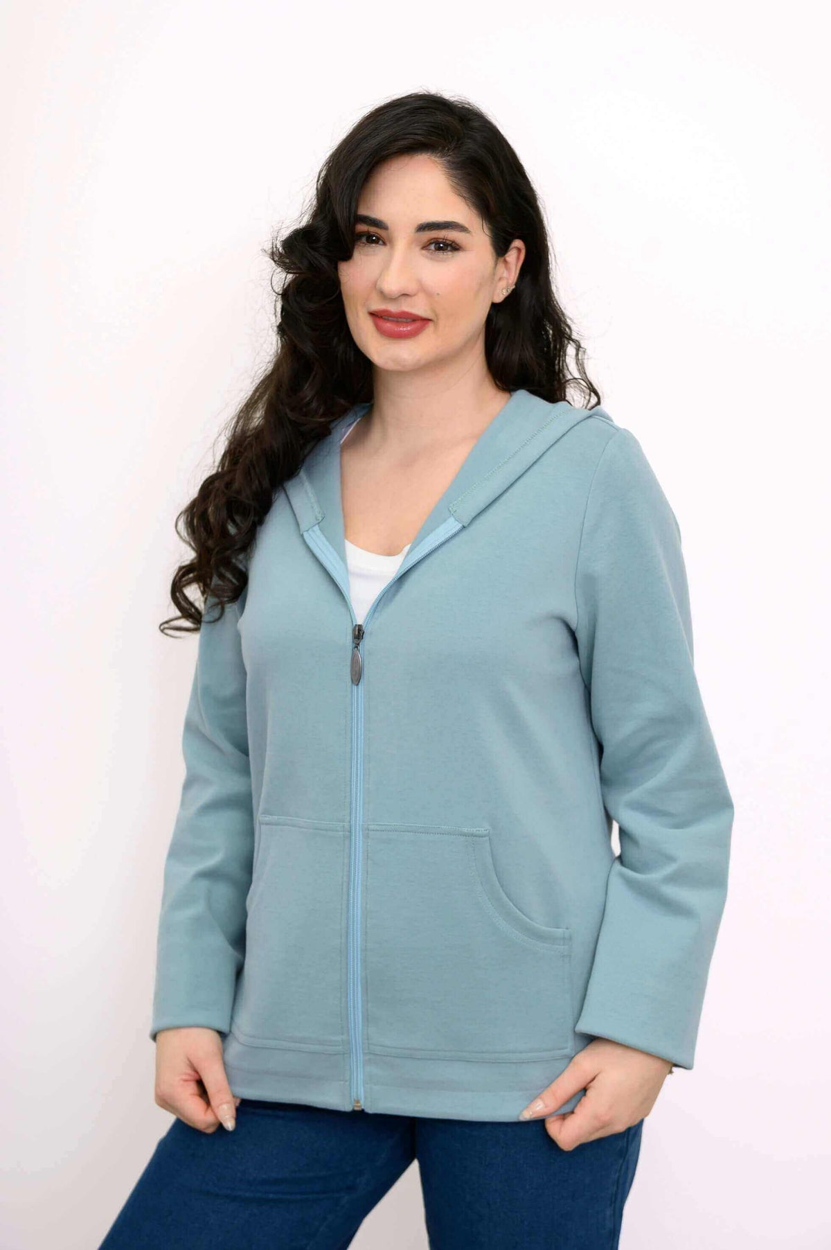 Woman in light blue hoodie jacket smiling and posing with hands in front pockets