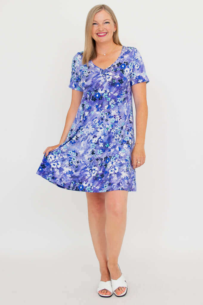 Woman holding skirt out, showing flow of violet floral V-neck dress
