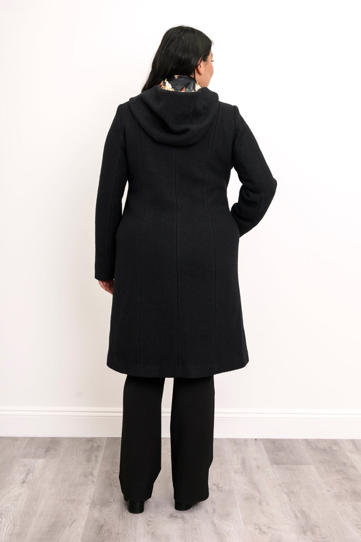 Back view of woman wearing knee-length figure hugging coat featuring black floral lining in the hood