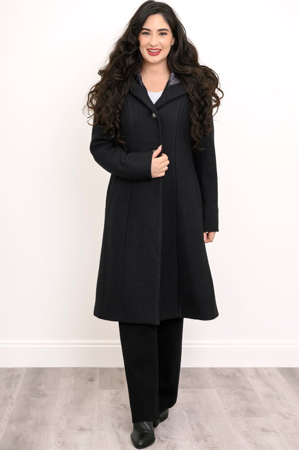 Woman wearing a long black coat, black pant, and black shoes on a white background, front view