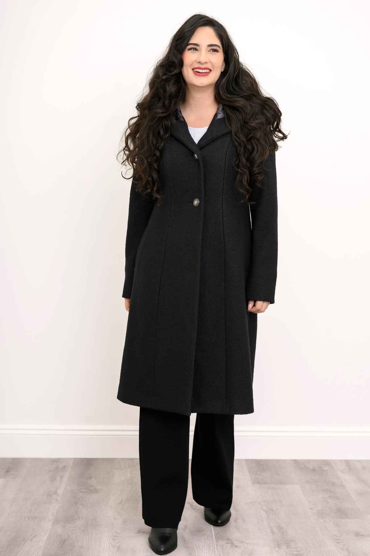 Full front view of woman smiling in long black wool coat with hood and silver buttons