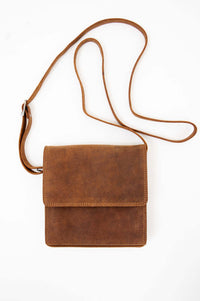 Brown leather crossbody bag with flap and adjustable strap on white background