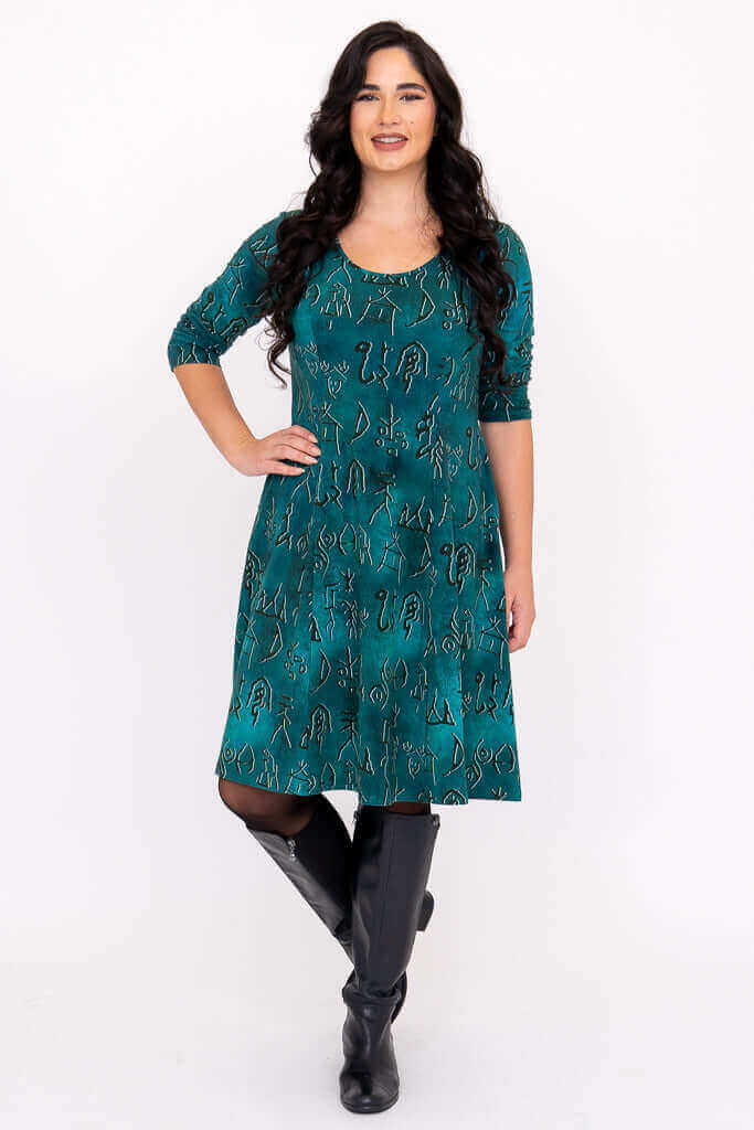 Woman in teal petroglyph print dress standing with her hand on her hip and smiling