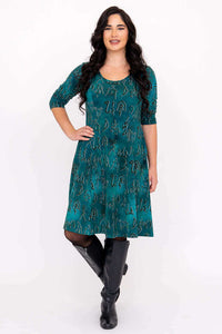 Woman in teal petroglyph print dress standing with her hand on her hip and smiling