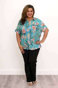 Woman in turquoise floral blouse paired with black pants and beige sandals