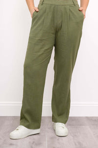 Close up front view of woman with her hands in the pockets of her olive green pleated trousers