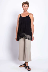 Woman modeling a black tank top with a lace hem, styled with wide-leg beige pants