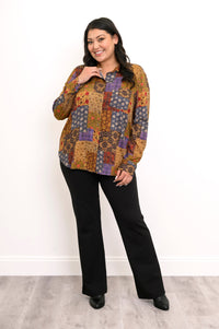 Woman wearing a colorful patchwork print shirt and black pants against a white background