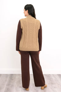 Back view of a honey-beige cable knit vest, highlighting the vertical sweater texture and straight, ribbed hemline.