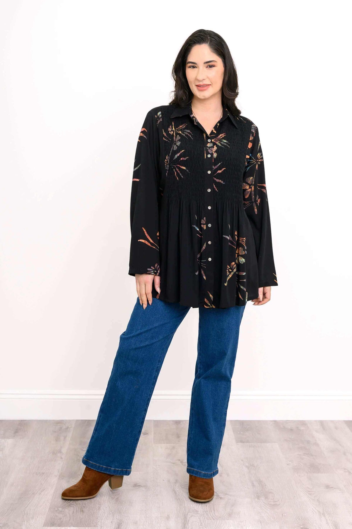 Woman wearing black smocked floral tunic shirt, facing forward in blue jeans