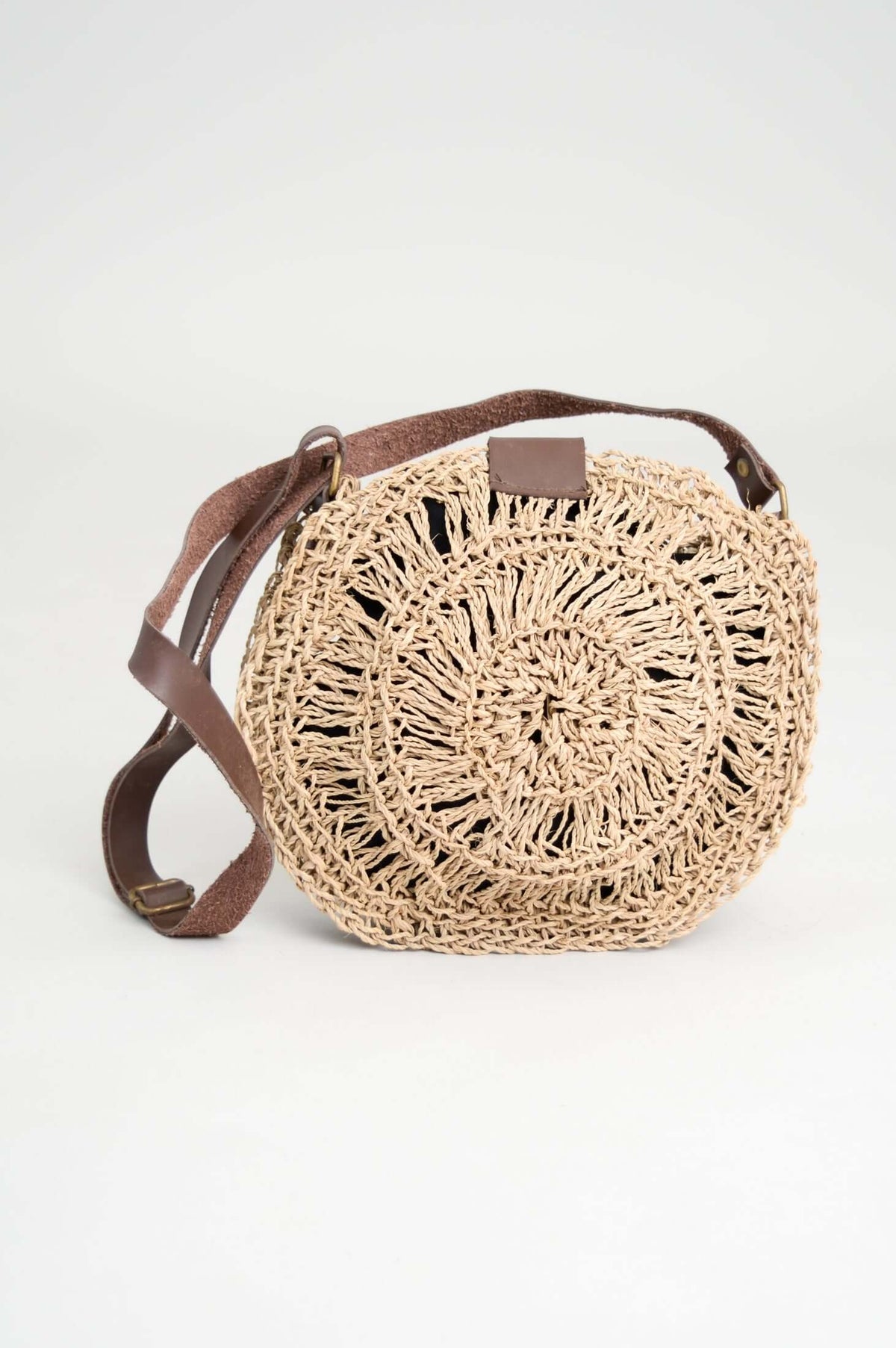 Circular handwoven rattan bag with adjustable brown leather strap, straight-on view