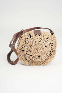 Circular handwoven rattan bag with adjustable brown leather strap, straight-on view