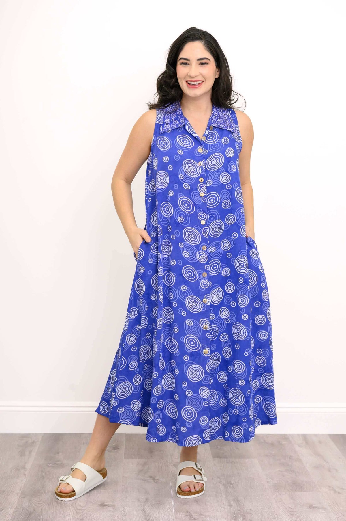 Smiling model with hand in pocket, in sleeveless blue dress with swirl pattern