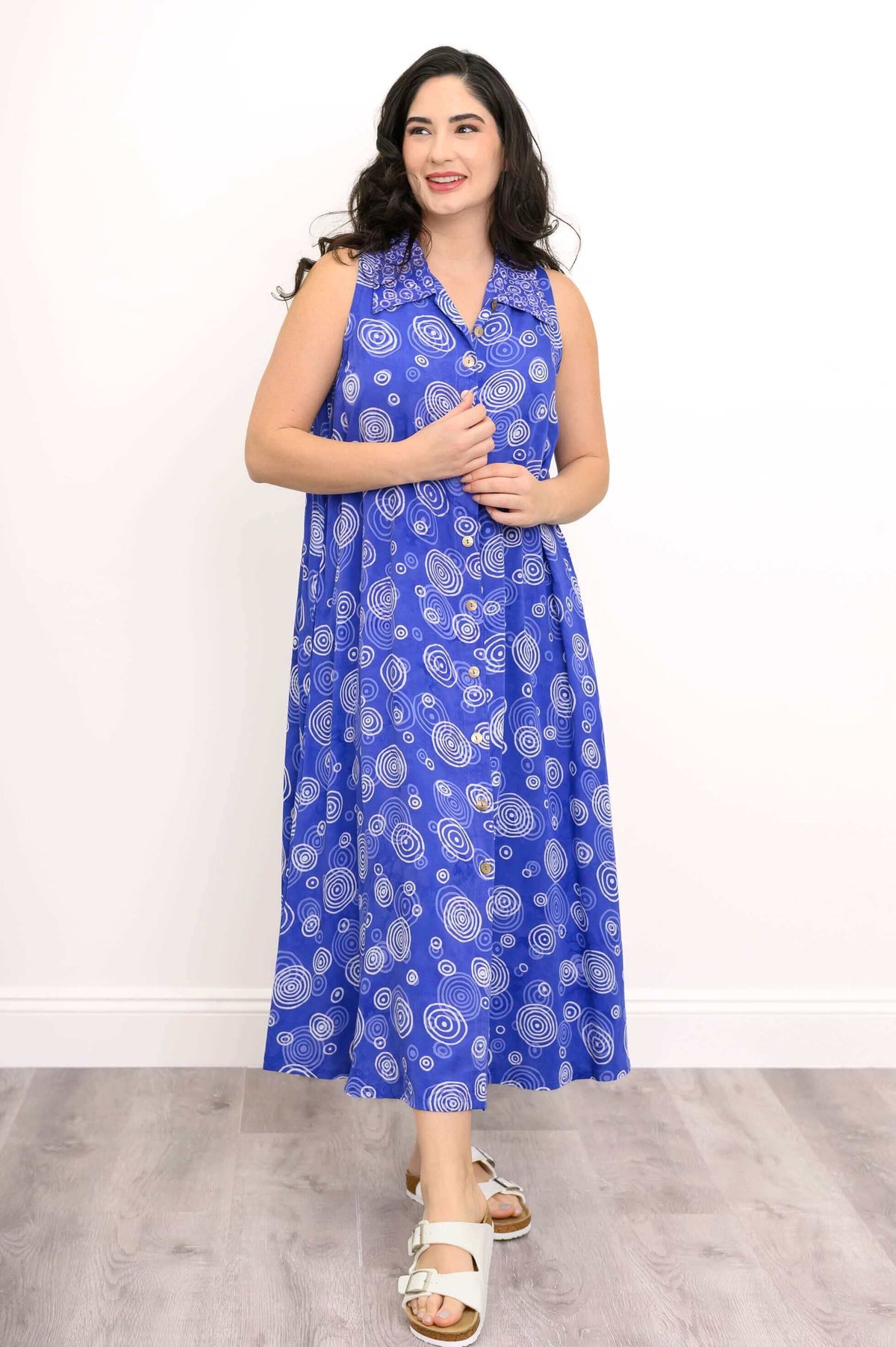 Model posing in sleeveless blue dress with white swirls and button front