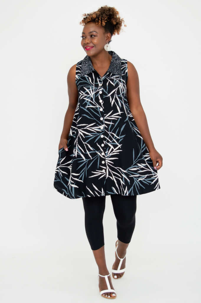 Model walking in black sleeveless leaf print button-up tunic top with leggings and sandals