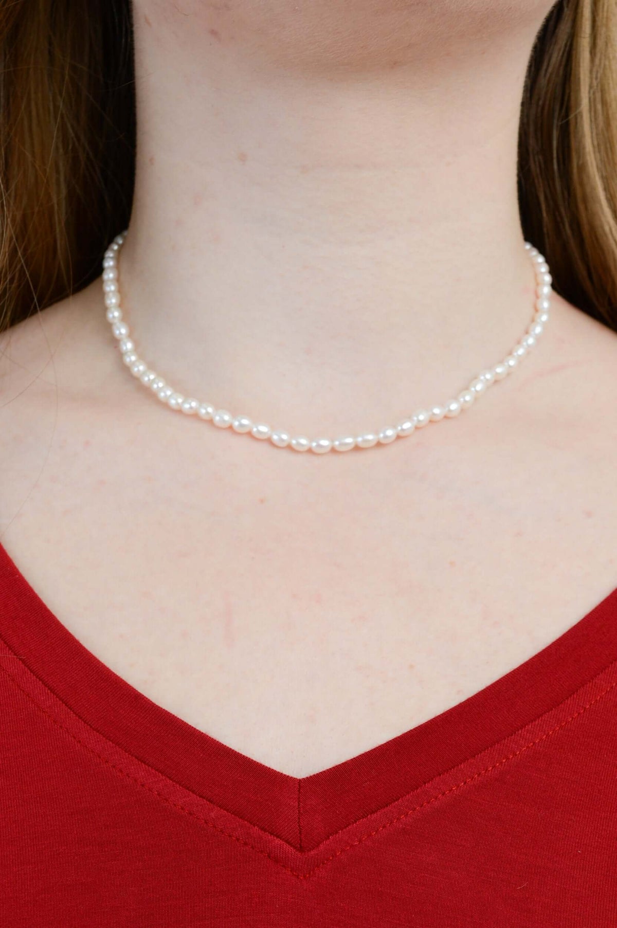Classic pearl necklace worn around the neck with a red V-neck top