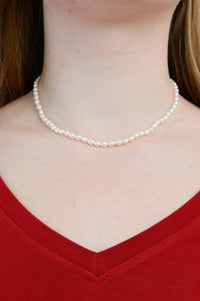 Classic pearl necklace worn around the neck with a red V-neck top