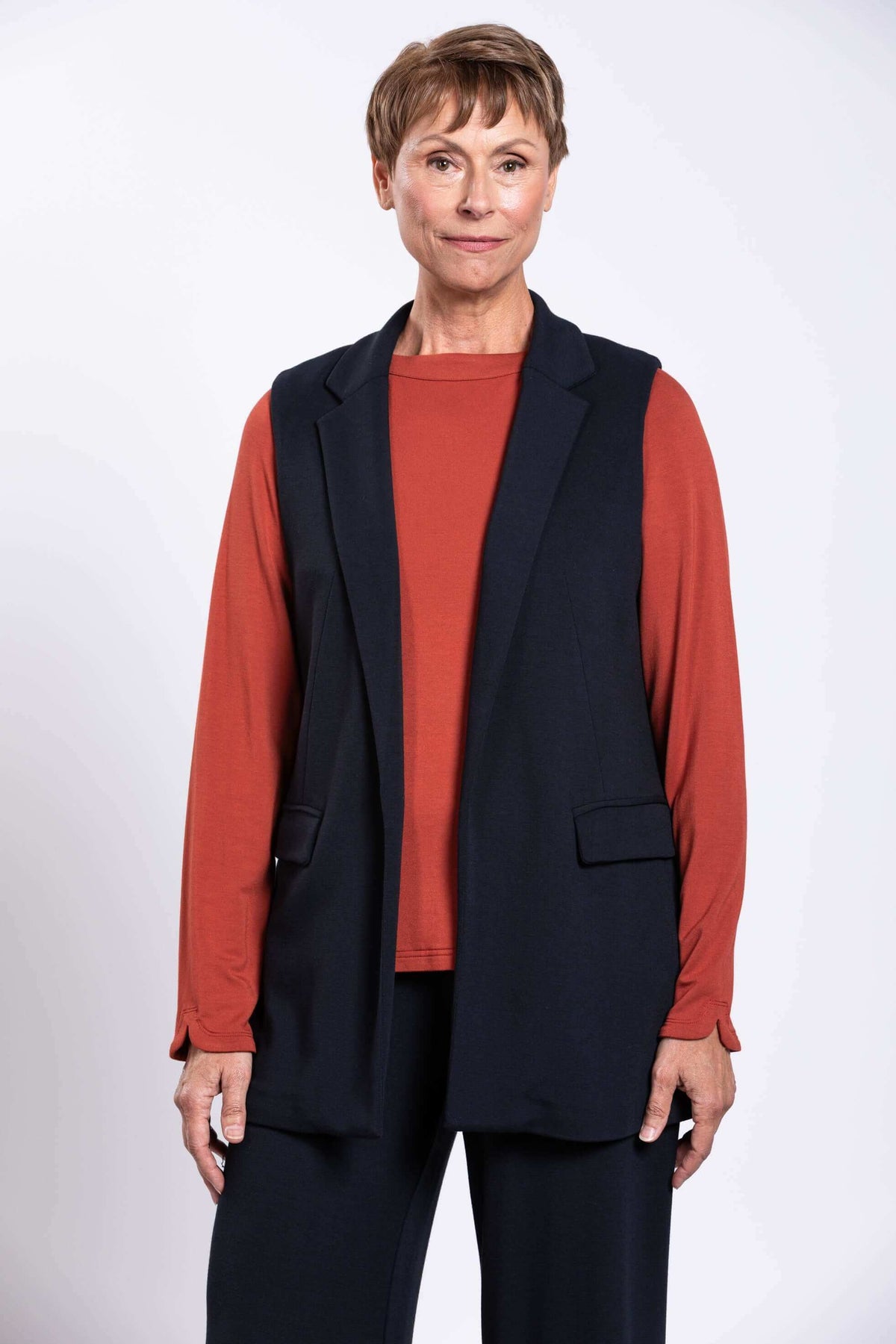 Close-up of model wearing black open front vest with notch collar and rust long sleeve top