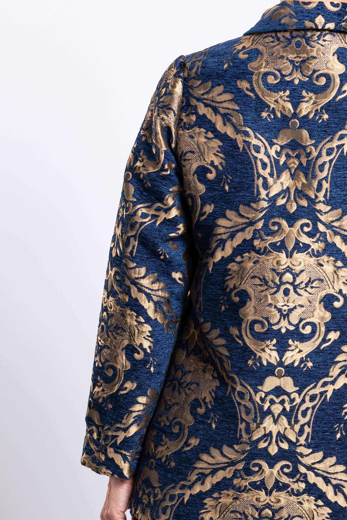 Close-up of jacquard fabric showing blue base and intricate gold pattern on coat sleeve and back