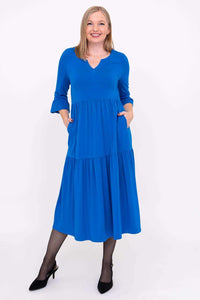 Front close-up of a woman in a blue midi dress showing tiered skirt and pockets