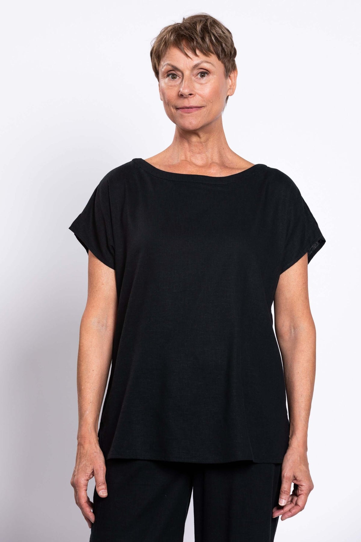 Close-up front view of a woman in a black linen blend tee with cap sleeves and a boatneck