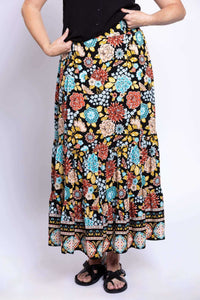 Close-up front view of a woman wearing a black, multi-color floral tiered maxi skirt