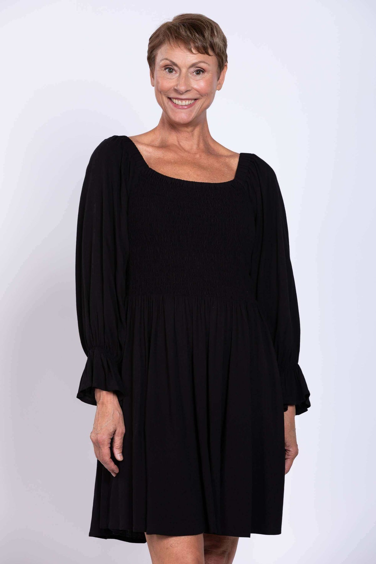 Close-up of a woman smiling in a black dress with smocked bodice and ruffled sleeves