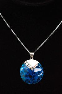 Close-up of sterling silver necklace with blue round pendant on black background