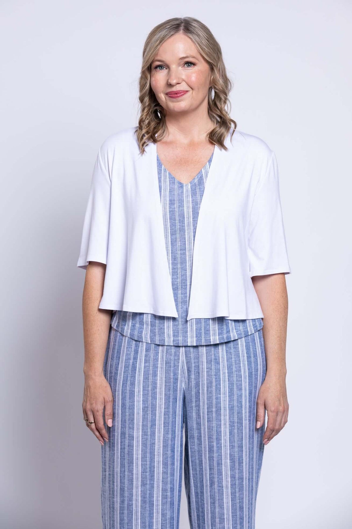 Close-up of woman wearing white cardigan over blue striped sleeveless top and capri pants