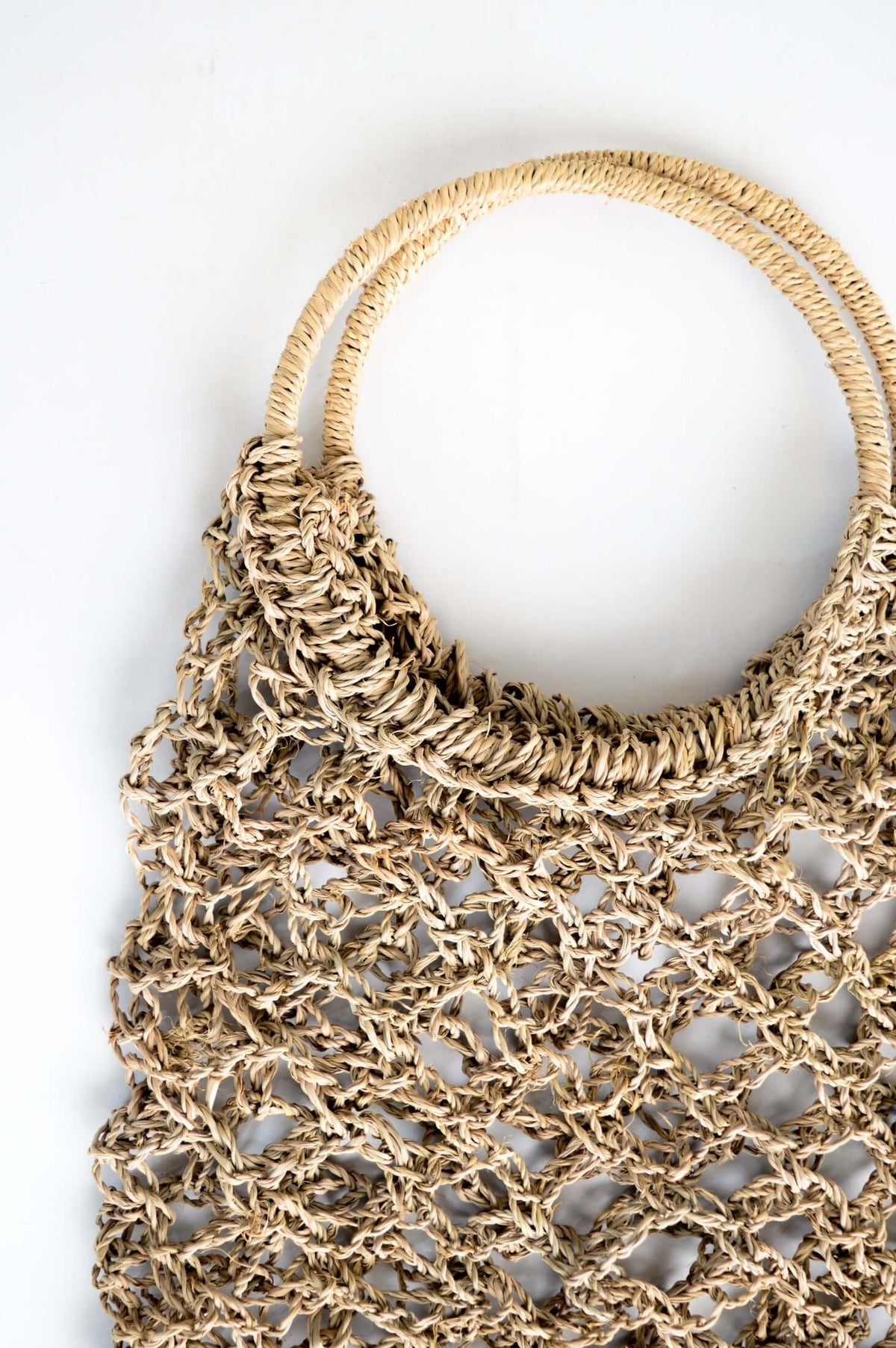 Close-up of hand woven rattan tote bag showing net weave and sturdy ring handles