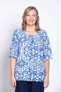 Close-up front view of a woman wearing a blue and white boho peasant top with a tile pattern