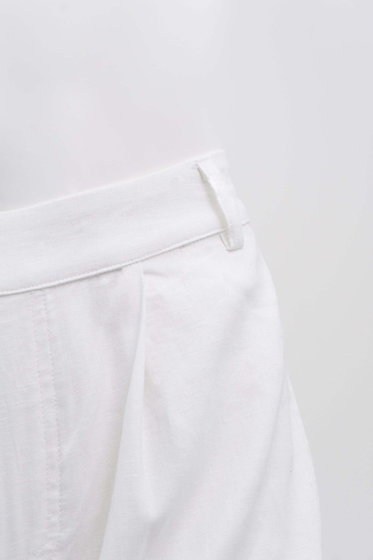 Close-up of waistband and pleat detail on a pair of white trousers