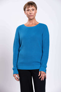 Closer front view of a woman in a blue cotton sweater and black pants