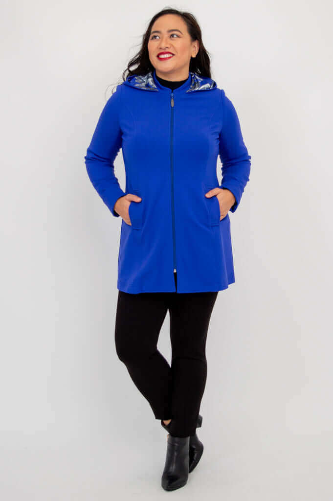 Woman in cobalt blue hooded coat looking to the side with hands in pockets