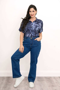 Woman in navy floral blouse with blue jeans, hand in pocket, standing confidently