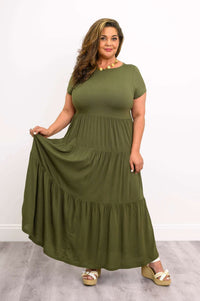 Curvy model wearing olive tiered maxi dress holding skirt hem
