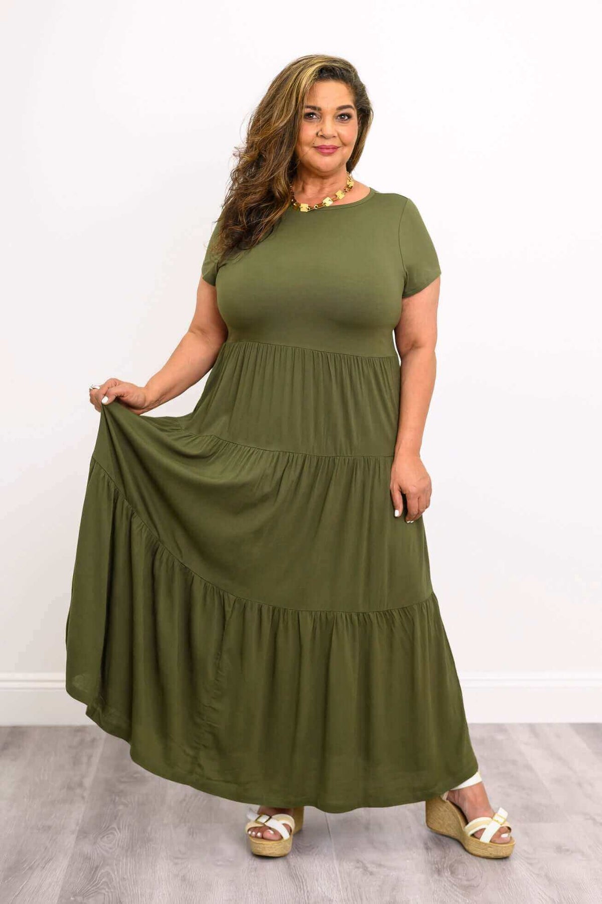 Curvy woman in olive green tiered maxi dress holding skirt hem, wearing sandals