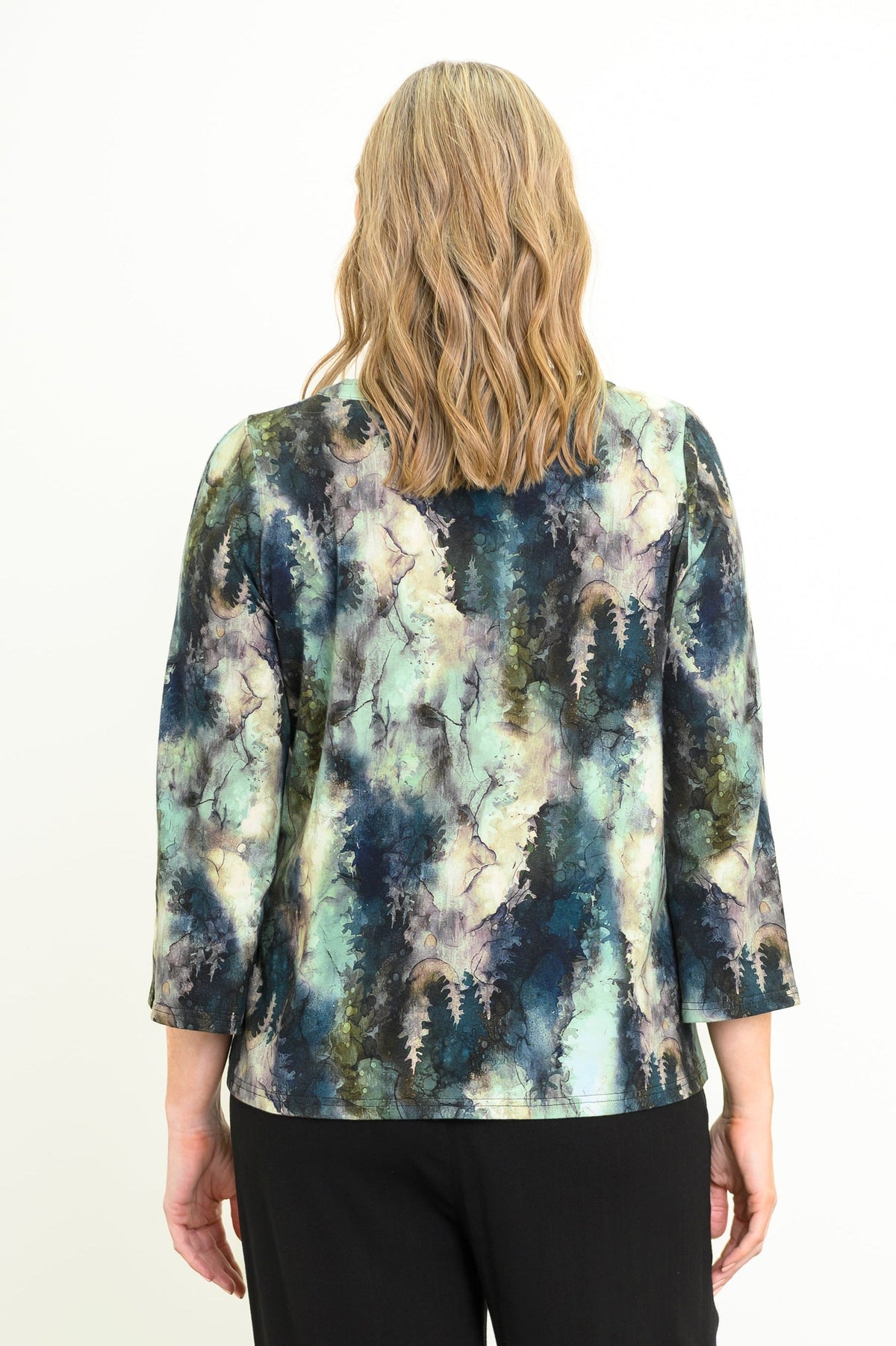 Back view of a women's green leaf patterned long-sleeve bamboo top styled with black pants.