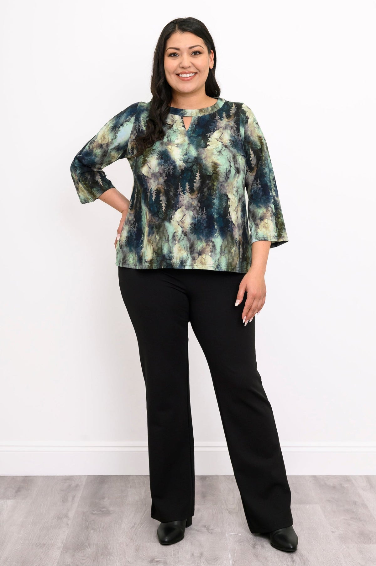 Full-body shot of a patterned green knit top with 3/4 bell sleeves and black trousers, showing the hip-length hem.