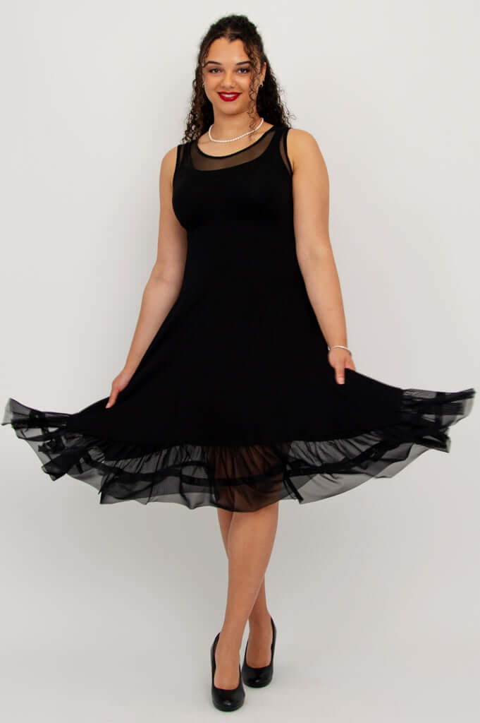 Model holding out skirt of black dress showing mesh layered hem