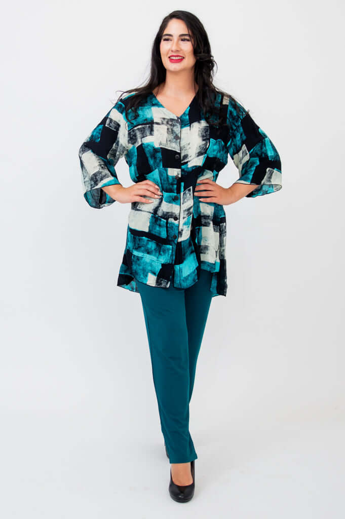 Woman standing with hands on hips in Darla blouse and teal pants, smiling